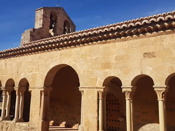 Galería porticada de piedra con arcos y espadaña.