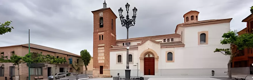 Plaza amplia con iglesia blanca, torre de ladrillo y farola central