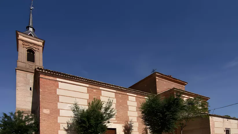 Iglesia de ladrillo con torre alta y árboles en la fachada