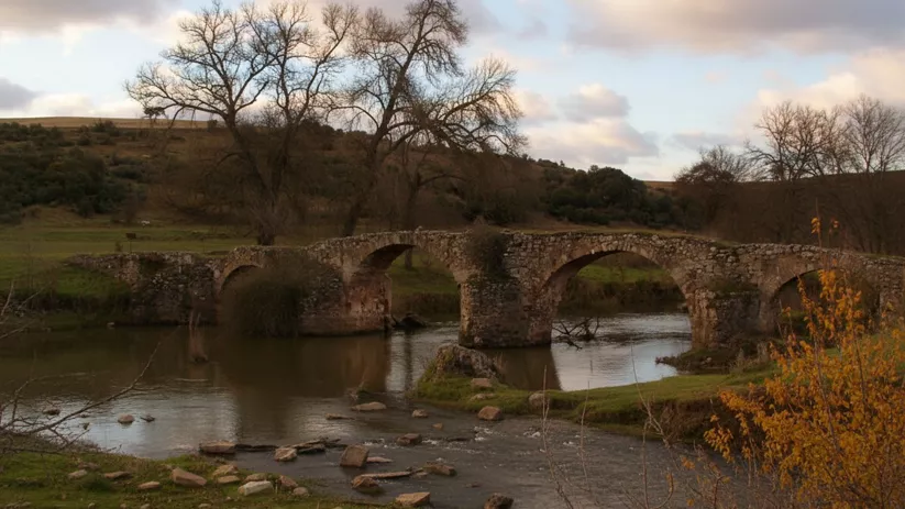 Puente medieval de piedra sobre el río en Los Pozuelos de Calatrava (Ciudad Real), paisaje natural al atardecer.