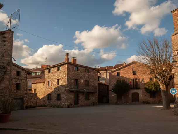 Plaza rural con casas de piedra y cielo parcialmente nuboso