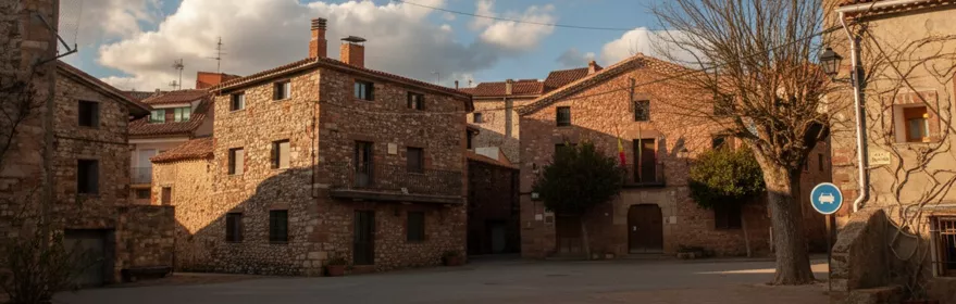Plaza rural con casas de piedra y cielo parcialmente nuboso