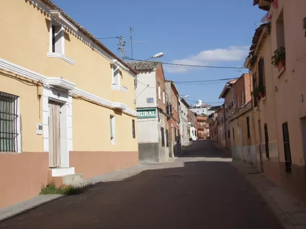 Calle estrecha y tranquila en un pueblo con edificios de fachadas en tonos amarillos y blancos bajo un cielo despejado.