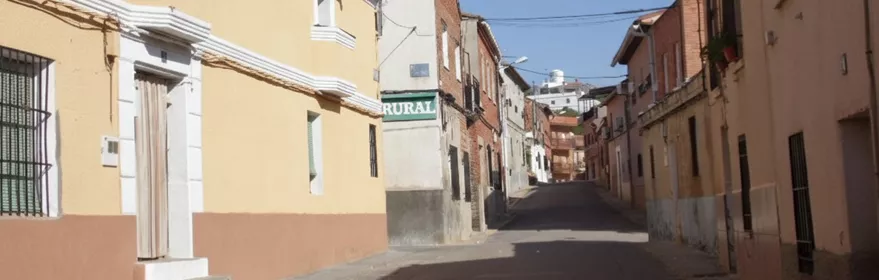 Calle estrecha y tranquila en un pueblo con edificios de fachadas en tonos amarillos y blancos bajo un cielo despejado.