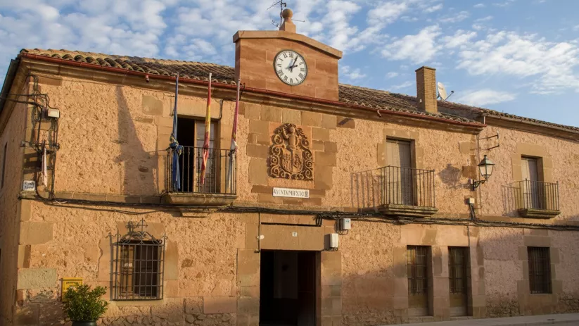 Edificio consistorial de piedra con reloj y balcones en una plaza tranquila.