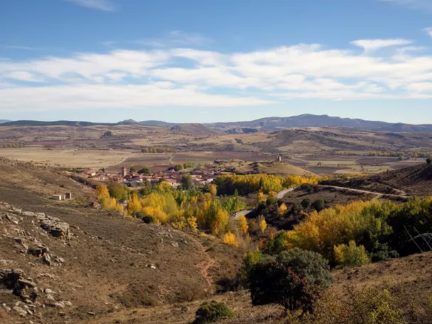 Vista panorámica de un pequeño pueblo rural rodeado de colinas y vegetación otoñal.