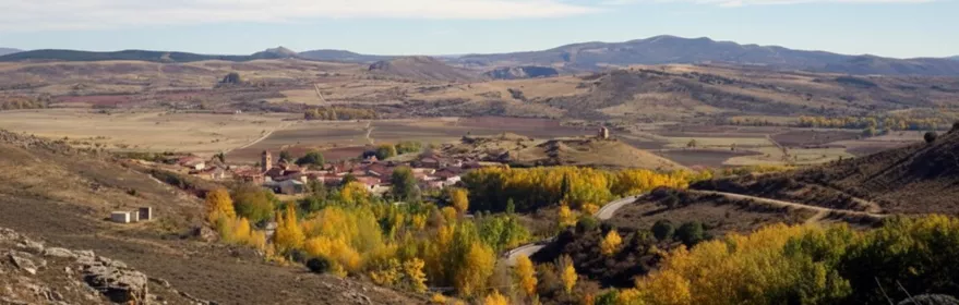 Vista panorámica de un pequeño pueblo rural rodeado de colinas y vegetación otoñal.