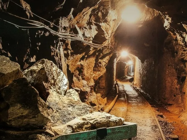 Galería minera con vías y roca iluminada.