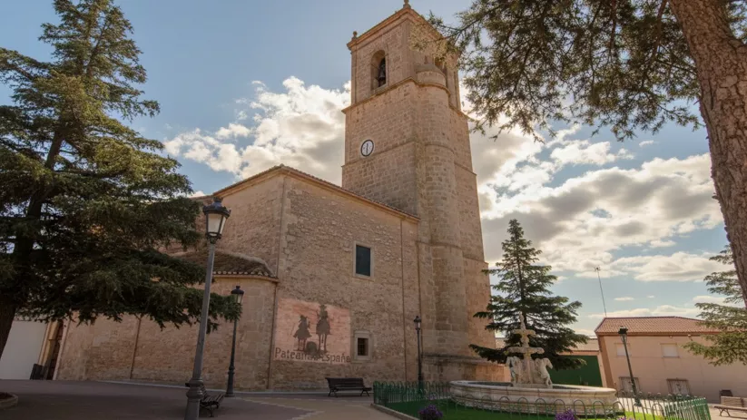 Iglesia parroquial de Minaya con torre, fuente ornamental y bancos en la plaza.