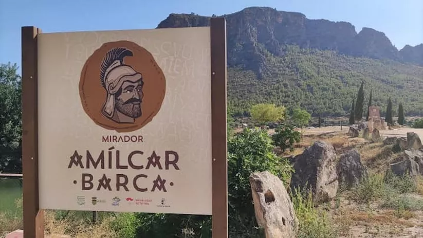 Cartel de mirador con ilustración de un guerrero y paisaje de montaña al fondo.