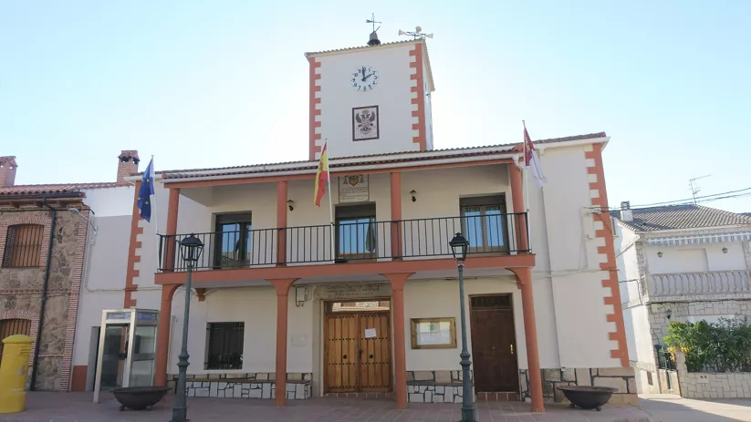 Fachada de ayuntamiento blanco con reloj, balcón y banderas