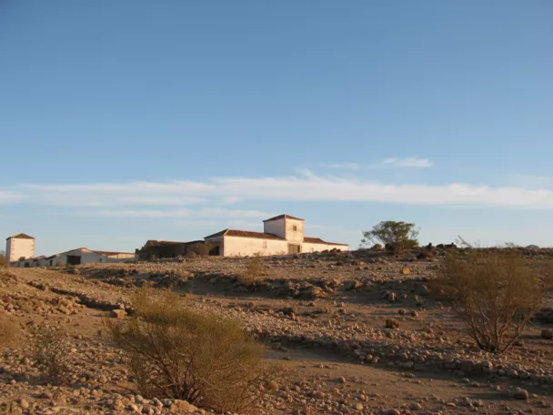 Caserío aislado sobre terreno pedregoso y seco bajo cielo azul.