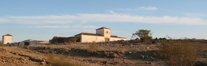 Caserío aislado sobre terreno pedregoso y seco bajo cielo azul.