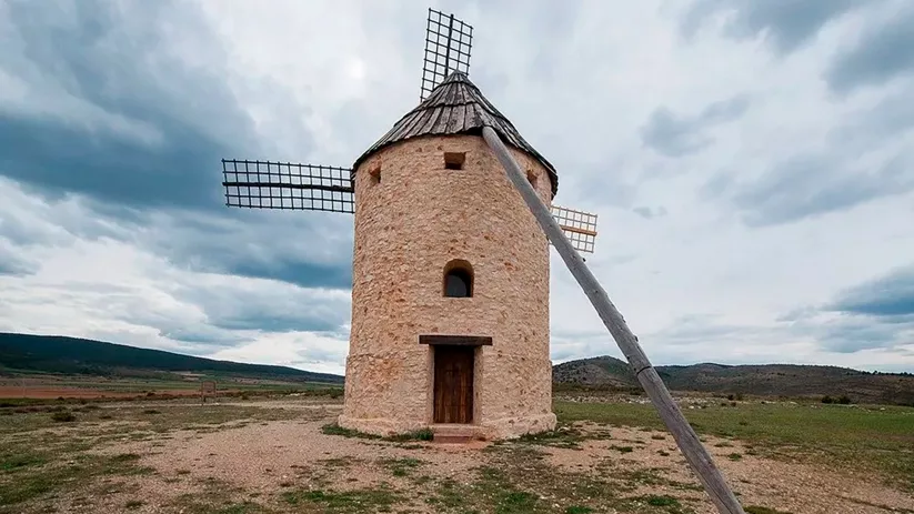 Molino de viento de piedra en campo abierto bajo cielo nublado.