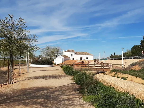 Camino rural con pasarela de madera y edificio tradicional blanco