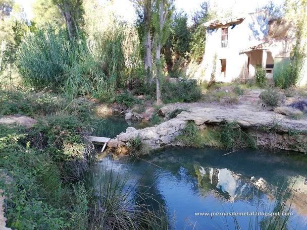 Manantial natural con agua clara junto a una pequeña construcción tradicional.
