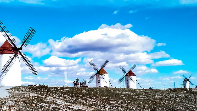 Molinos de viento blancos alineados sobre una colina bajo un cielo azul con nubes.