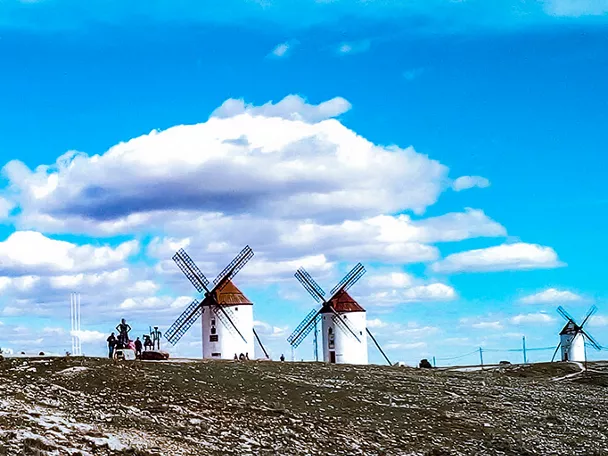 Molinos de viento blancos alineados sobre una colina bajo un cielo azul con nubes.