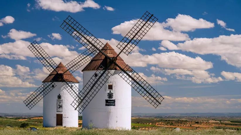 Vista lateral de varios molinos de viento con estructuras y esculturas cercanas.