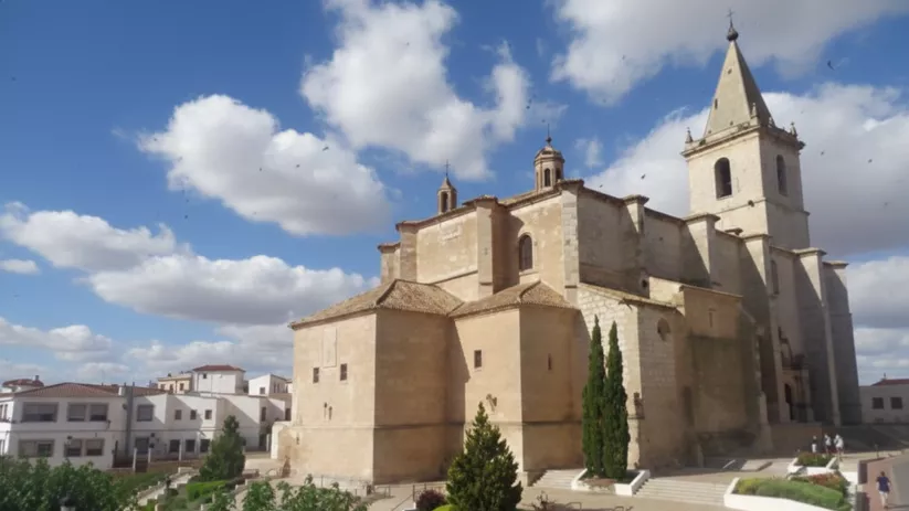 Iglesia parroquial de Montalvos de grandes dimensiones en piedra clara bajo un cielo azul con nubes.