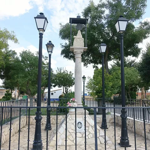 Monumento religioso rodeado de farolas en una plaza ajardinada