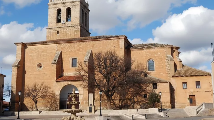 Iglesia parroquial de Motilleja en piedra dorada con torre campanario y plaza amplia.