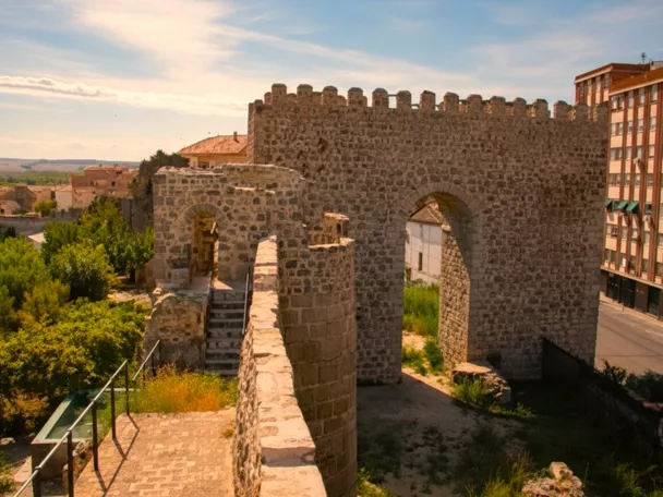Vista desde el adarve hacia una puerta almenada y escaleras de piedra, con vegetación alrededor.