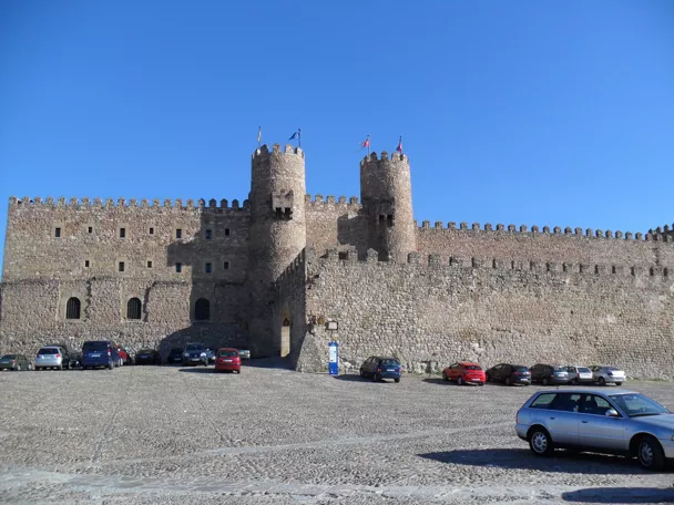 Muralla almenada con torres sobre plaza empedrada.