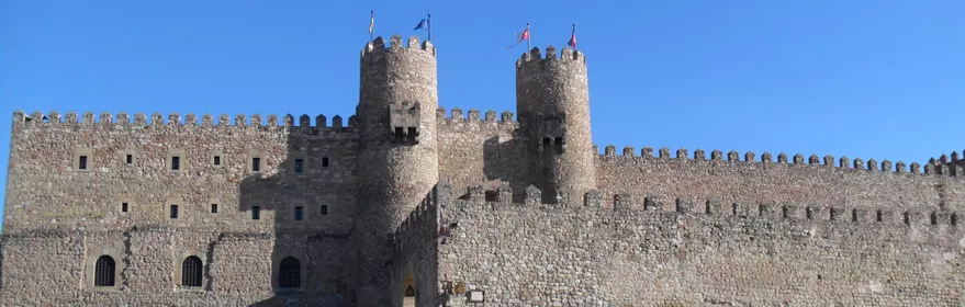 Muralla almenada con torres sobre plaza empedrada.