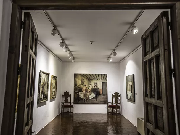 Sala de exposición con cuadros y mobiliario histórico iluminado