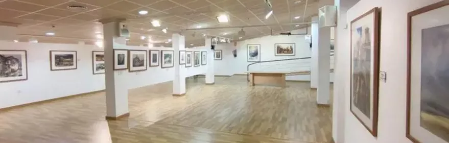 Sala amplia de exposiciones con suelo de madera y cuadros enmarcados.