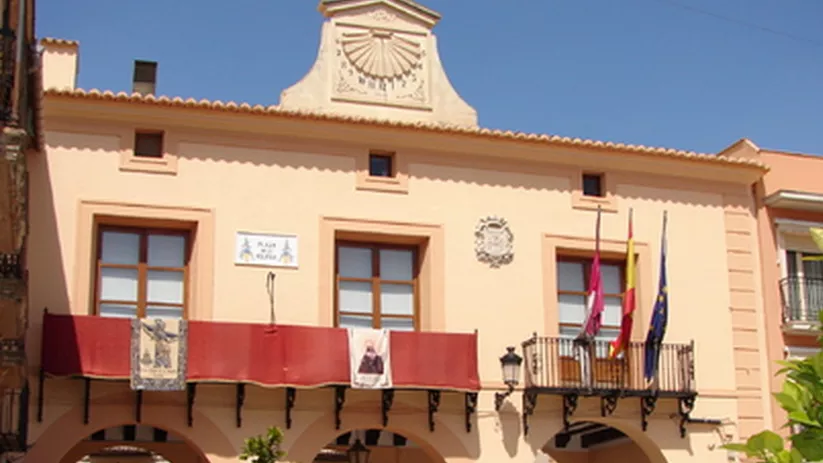 Fachada de edificio institucional con arcos, balcones y banderas.