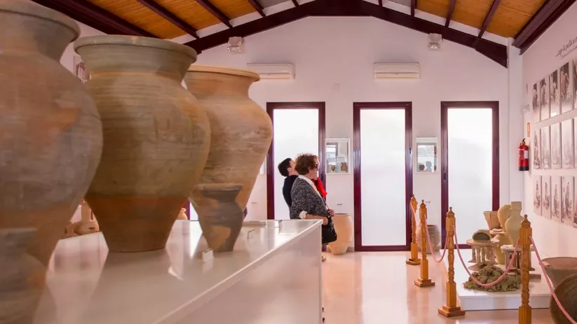 Sala de museo con grandes tinajas de barro y visitantes observando la exposición.