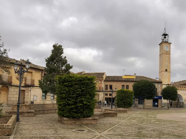 Plaza amplia con edificios históricos, torre del reloj y fachadas de ladrillo bajo cielo nublado.