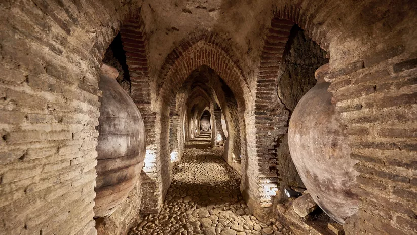 Galería subterránea con arcos de ladrillo y grandes tinajas de barro.