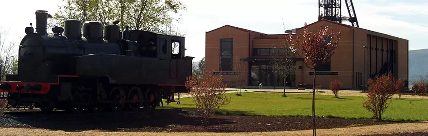 Locomotora minera histórica expuesta al aire libre junto a un edificio industrial restaurado y una torre metálica