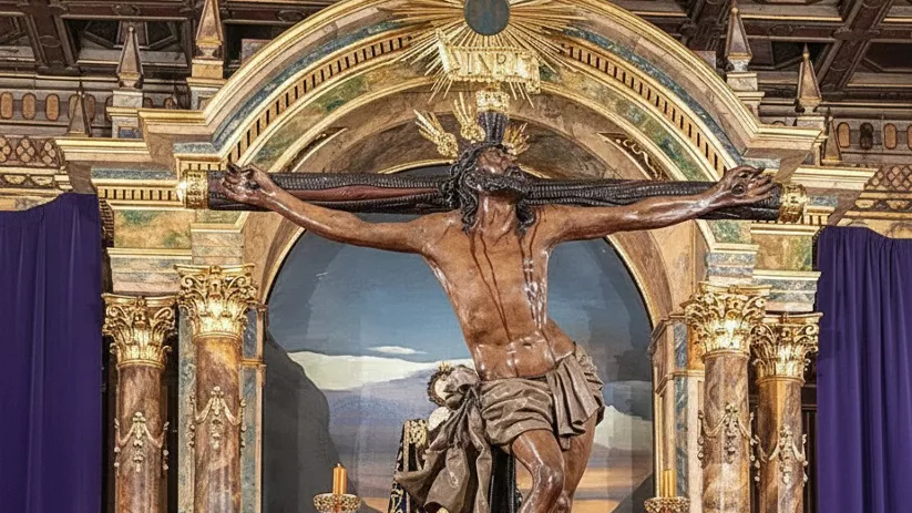 Paso procesional con Cristo crucificado, figuras secundarias, abundantes flores rojas y decoración dorada en interior de templo.