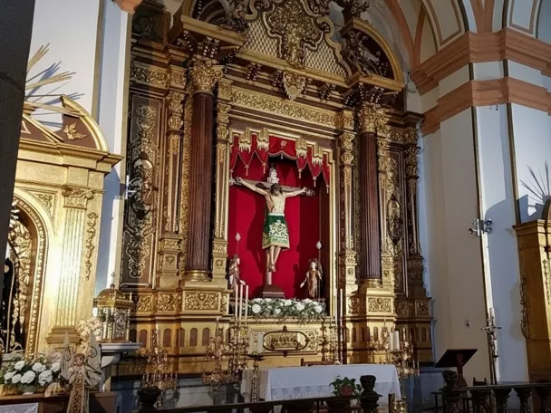 Retablo barroco dorado con imagen de Cristo crucificado sobre fondo rojo en el interior de una iglesia.