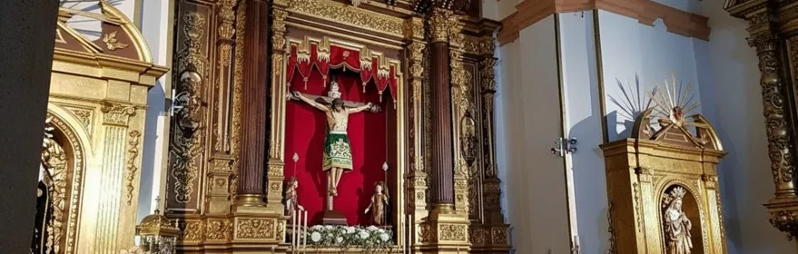 Retablo barroco dorado con imagen de Cristo crucificado sobre fondo rojo en el interior de una iglesia.