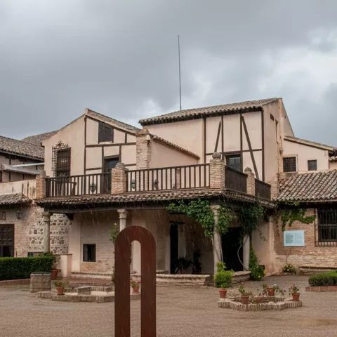 Fachada de edificio tradicional con patio ajardinado en día nublado.