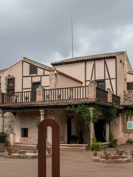 Fachada de edificio tradicional con patio ajardinado en día nublado.