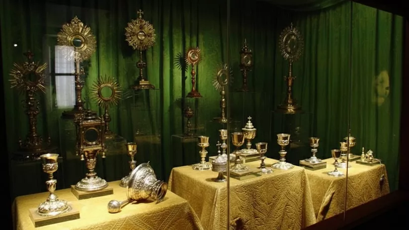 Vitrina con piezas litúrgicas doradas sobre tela verde.