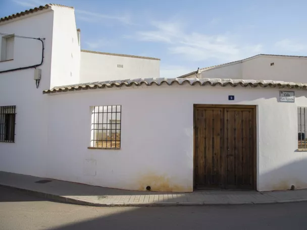 Fachada encalada en esquina con puerta de madera y ventanas con rejas.
