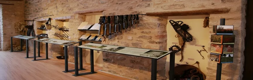 Sala expositiva con herramientas tradicionales sobre muros de piedra.