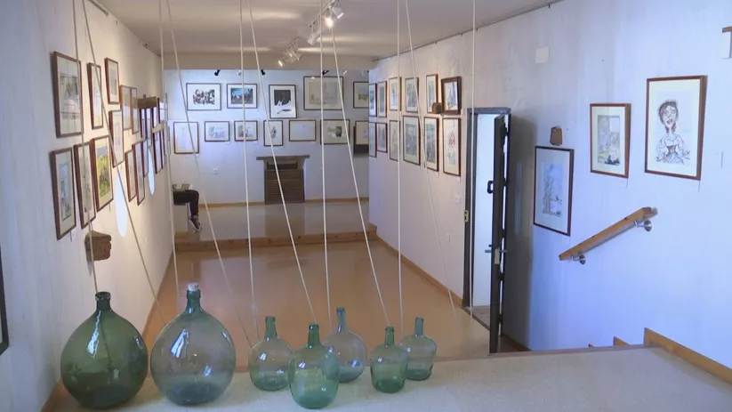 Galería con botellas de vidrio en primer plano y obras colgadas en las paredes.