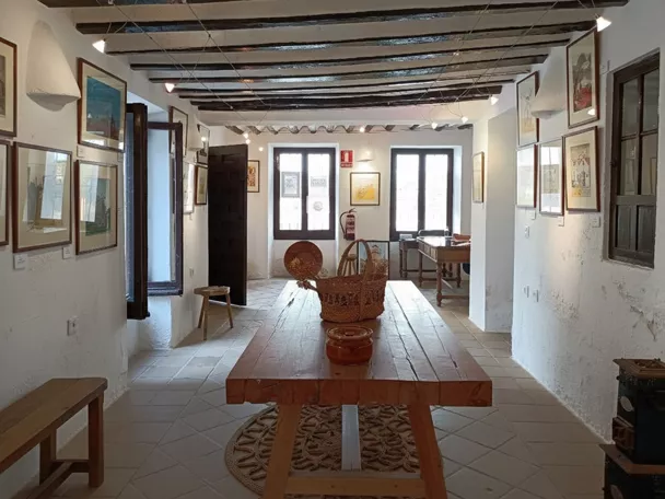 Interior con vigas de madera, mesa central y paredes cubiertas de dibujos.