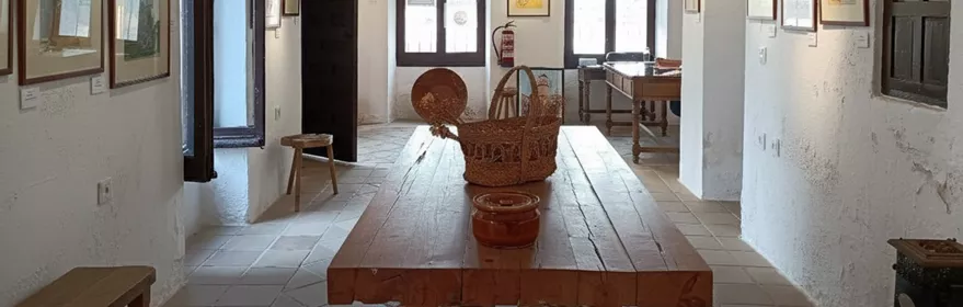 Interior con vigas de madera, mesa central y paredes cubiertas de dibujos.