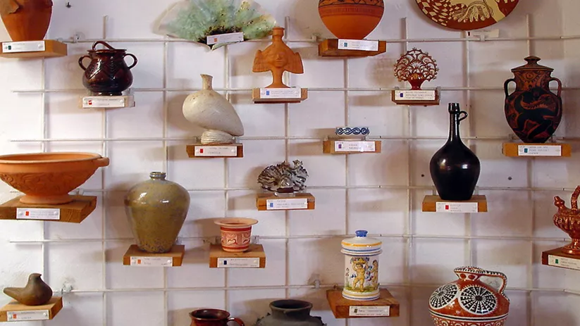 Muro expositivo con cerámicas decorativas y funcionales colocadas en soportes individuales.