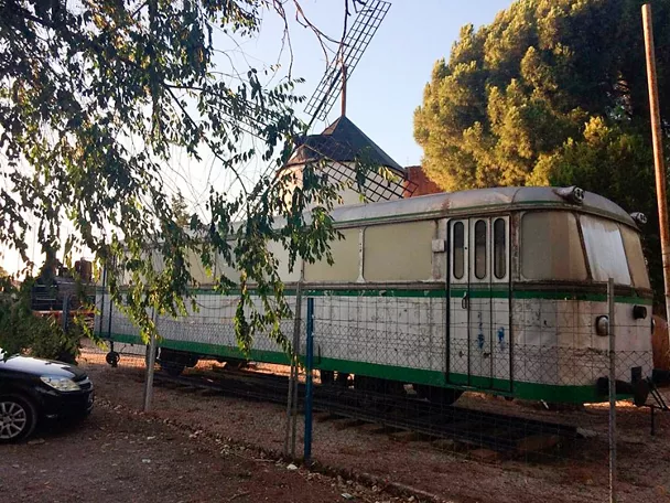 Vagón ferroviario histórico junto a un molino de viento.