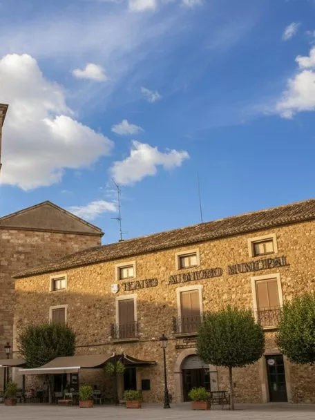 Plaza con torre de piedra y edificio histórico bajo cielo azul con nubes.